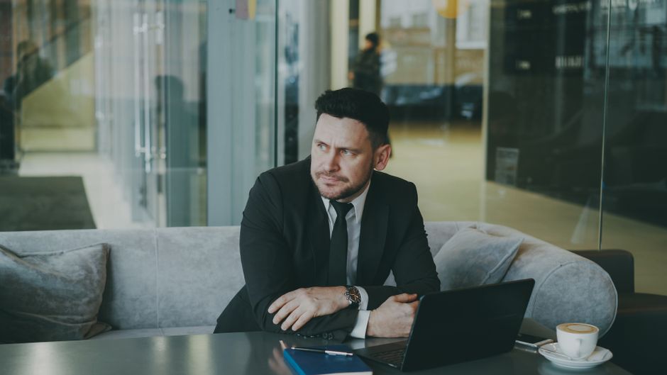 Person in mid-career writing notes at a desk with laptop and coffee