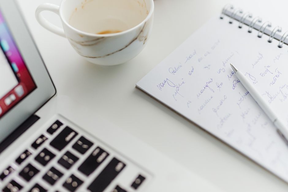Person writing a cover letter at a desk with laptop and notebook