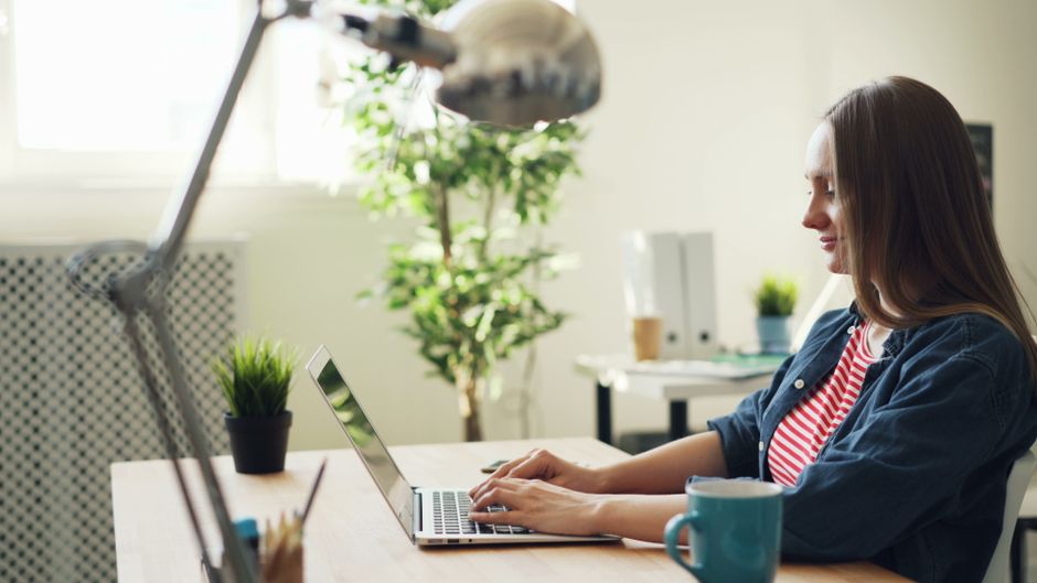 Mãos digitando em teclado com tela de vagas de emprego ao fundo
